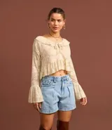 Short de jean estilo baggy con corte holgado, cintura alta, pliegues delanteros, bolsillos laterales y traseros, y trabillas para cinturón. Presenta un detalle de estampado vichy en el interior de la cintura.