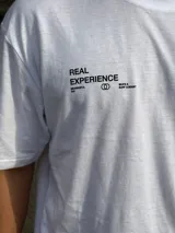 Remera blanca de corte oversize con estampado en la espalda que incluye dos círculos intersecados con las palabras 'Surf', 'Life' y 'Skate', y las frases 'Real Experience', 'Coexist' y 'Meaningful Day'.