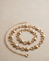 Cinto de metal dorado con diseño de eslabones articulados combinados con piezas circulares y herrajes geométricos. Cuenta con una tira colgante de cadena terminada en un dije redondo.