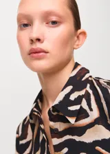 Camisa de poliéster con estampado animal print tipo cebra en tonos negro, marrón y beige, manga larga y cuello camisero clásico.