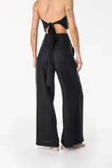Pantalón de lino blanco de corte ancho y fluido, con cintura alta que incorpora una sobrepretina ancha desmontable con pliegues horizontales.