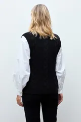 Chaleco tejido de punto color lacre, con cuello redondo, cierre frontal con botones y diseño de trenzas laterales.