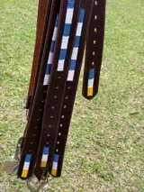 Cinturón de cuero marrón con detalle de bordado en los colores de la bandera de Uruguay (azul, blanco y amarillo). Cuenta con hebilla metálica y múltiples perforaciones para ajuste.