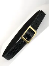 Cinto de cuero negro con textura de reptil, hebilla circular metálica en tono bronce envejecido y detalles de remaches metálicos.