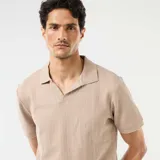 Remera polo de manga corta en color beige, confeccionada en tejido con textura de nido de abeja, con cuello camisero y escote en V.