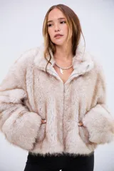 Campera de piel sintética en tono beige con textura suave y voluminosa. Presenta cuello alto, cierre frontal completo y mangas largas con puños amplios.