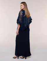 Vestido largo azul marino de seda fría, compuesto por una falda recta con tajo frontal y una capa superior superpuesta de encaje con lentejuelas bordadas, escote a la base y mangas tres cuartos acampanadas.
