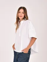 Blusa blanca de manga corta, con cuello camisero y abertura frontal parcial con botones. Presenta un corte holgado y bajo redondeado.