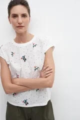 Blusa blanca con bordados florales y broderie en el frente, de manga corta y corte recto.