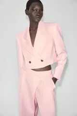 Blazer corto rosado con cuello solapa, hombreras y mangas largas. Cuenta con cierre cruzado delantero con dos botones oscuros y un bolsillo de ojal en el pecho.