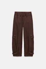 Pantalón cargo de tiro medio confeccionado en algodón, con diseño de pierna ancha y costuras verticales. Presenta bolsillos laterales y bolsillos de plastrón con solapa en las piernas. El bajo es ajustable mediante trabillas y hebillas metálicas.