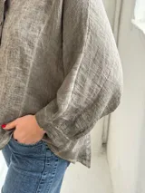 Camisa de lino color visón, de corte holgado, con cuello mao y cierre frontal de botones.