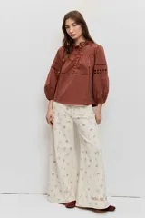 Camisa de manga larga abullonada color marrón, con detalles de bordados calados en el pecho y las mangas, y cierre frontal con botones.