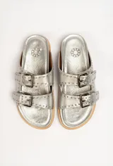 Sandalias de cuero color negro con dos tiras anchas sobre el empeine, cada una con hebillas metálicas ajustables y detalles de tachas plateadas. La suela es de cuero con un borde de color madera.