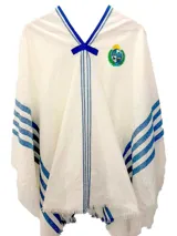 Poncho de tejido liviano en color blanco con detalles de franjas verticales en azul y escudo nacional bordado en el pecho. Presenta terminaciones con flecos en el ruedo y un lazo decorativo en el cuello.