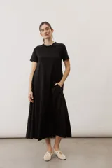 Vestido midi negro con diseño de manga corta, cuello redondo y bolsillos laterales, corte amplio y fluido.