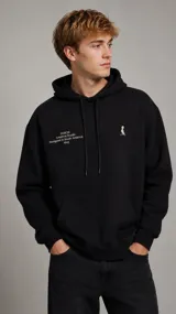 Hoodie negro con capucha y cordones ajustables, bolsillo frontal tipo canguro, puños y dobladillo elásticos. Presenta texto estampado en el pecho derecho y un pequeño logotipo en el izquierdo.