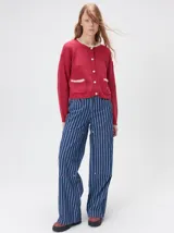 Cardigan de algodón grueso color rojo, con cuello redondo, cierre frontal de botones grandes y bolsillos cuadrados en el frente. Presenta detalles de pelo sintético en el cuello y los bolsillos, y logo bordado en uno de los bolsillos.