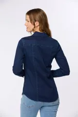 Camisa de jean celeste con lycra, corte entallado, cuello camisero, cierre frontal con botones a presión, dos bolsillos con solapa abotonada en el pecho y mangas largas con puños abotonados.