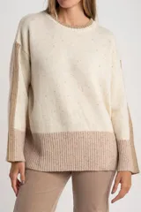Sweater de lana color crema con efecto tweed, de calce oversize y cuello redondo. Presenta bloques de color en la parte inferior, puños y laterales de las mangas en tono beige con textura acanalada y detalles brillantes.