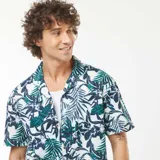 Camisa de manga corta con estampado de hojas y flores en tonos verde, azul y blanco. Tiene cuello clásico y cierre frontal con botones.