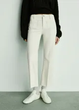 Jeans de tiro medio color blanco roto, estilo acampanado, con bolsillos de parche delanteros y traseros, trabillas para cinturón y cierre frontal con cremallera y botón.