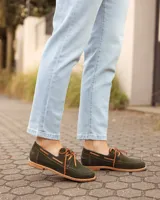 Zapatos náuticos de cuero verde oscuro, estilo mocasín con cordones de cuero marrón claro, costuras visibles en contraste y suela plana.