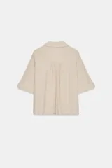 Camisa negra de textura arrugada, con cuello solapa, escote en V y cierre frontal de botones. Cuenta con mangas cortas terminadas en vuelta con trabilla y botón.