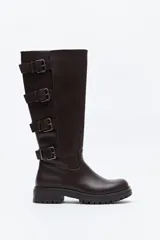 Bota de caña alta tipo biker en símil cuero color marrón oscuro. Presenta múltiples tiras horizontales con hebillas metálicas laterales y una suela robusta con relieve.