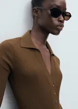 Jersey de punto fino color marrón, con cuello camisero, manga corta y cierre frontal con botones pequeños.