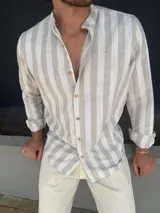 Camisa de manga larga con cuello mao, confeccionada en tejido símil lino con diseño de rayas verticales en tonos beige y blanco. Presenta cierre frontal con botones de madera y puños con doblez.
