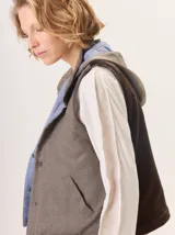 Chaleco con capucha, presenta una espalda de pelo sintético en color marrón oscuro con etiqueta de cuero negra y una capucha de tela tipo denim azul. Diseño original con mezcla de texturas.