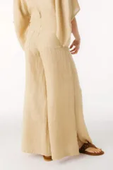 Pantalón ancho de tiro alto, color beige claro, confeccionado en lino. Presenta costuras verticales marcadas en el frente de cada pierna y cierre frontal con botón.