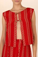 Chaleco rojo con estampado de cadenas doradas, sin mangas y con cuello redondo. Cierre frontal con ojales, botones dorados y cordones entrelazados.