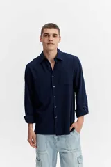 Camisa rústica de manga larga color azul marino, con textura natural, cuello clásico, cierre frontal con botones y un bolsillo aplicado en el pecho.