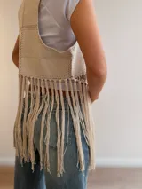 Chaleco de diseño patchwork en tonos neutros con efecto gamuza y pespuntes decorativos, abierto al frente y con largos flecos colgantes en el bajo.