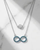 Collar doble de plata 925, compuesto por una cadena superior con dije de punto de luz y una cadena inferior con dije en forma de símbolo de infinito decorado con circonias turquesas.