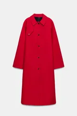 Trench largo color rojo de la línea ZW Collection de Zara, con cuello solapa, manga larga y bolsillos laterales ocultos. Presenta un diseño con forro interior a contraste y cierre frontal con botones a presión.