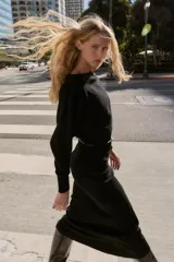 Vestido midi de punto en color negro, con cuello barco y mangas largas con sisa ancha. Presenta una cintura entallada con un cinturón fino incorporado con hebilla metálica dorada.