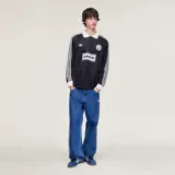 Camiseta Adidas de manga larga en colaboración con la banda Oasis, de color negro con cuello polo, puños y detalles en blanco marfil. Presenta las tres tiras características en las mangas, el logo trébol de Adidas, un escudo circular conmemorativo de la gira 'Live '25' y el estampado con la inscripción 'oasis' en el centro del pecho.