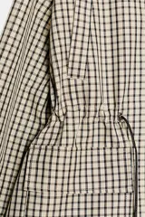 Chaqueta de corte holgado con estampado de cuadros, cuello subido, manga larga con puños elásticos y cintura ajustable mediante cordones. Presenta bolsillos delanteros con solapa y cierre frontal con cremallera oculta y botones a presión.
