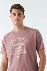 Remera color ladrillo con estampado frontal con la leyenda "BROOKSFIELD CLASSIC BRAND COMPANY TRADE MARK BASED IN TORINO - ITALY - ROAD MARKET EST 1971 REG TM".