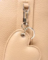 Cartera mediana XL color beige de símil cuero con textura granulada, doble asa de mano, correa ajustable y desmontable, y detalle de llavero en forma de corazón.
