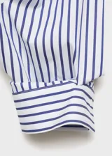 Camisa crop de corte recto confeccionada en mezcla de algodón, poliéster y viscosa. Presenta diseño de rayas verticales en azul y blanco, cuello camisero, bolsillo aplicado en el pecho y cierre delantero con botones.