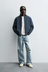 Cazadora bomber ligera de tejido técnico color verde oliva, con cuello, puños y bajo en rib elástico. Presenta cierre frontal de cremallera y bolsillos de vivo en la cadera.