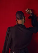 Blusa negra de viscosa con cuello redondo, detalle de fular anudado al cuello y volantes. Presenta mangas largas con puños abotonados y cierre frontal con botones.