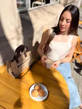 Cartera tipo tote de cuero color beige, con doble asa corta marrón y cierre superior con cremallera. Tiene un bolsillo frontal con cremallera y forro interior de tela con un bolsillo.