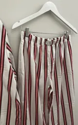 Conjunto de pijama de dos piezas compuesto por una camisa de manga larga con botones frontales y un pantalón de corte holgado, ambos con estampado de rayas verticales en tonos azul y blanco. El pantalón cuenta con un detalle de vivo en color oscuro en el ruedo.