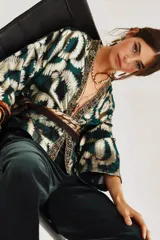 Kimono de manga ancha con estampado abstracto en tonos verde esmeralda, negro y dorado metalizado (lurex). Presenta un ribete decorativo en el escote y el frente, y se ata a la cintura con un fajín estampado.