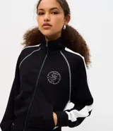Campera deportiva de cuello alto y cierre frontal, color negro con franjas blancas en las mangas y costuras decorativas contrastantes. Cuenta con bolsillos laterales y puños ajustados.